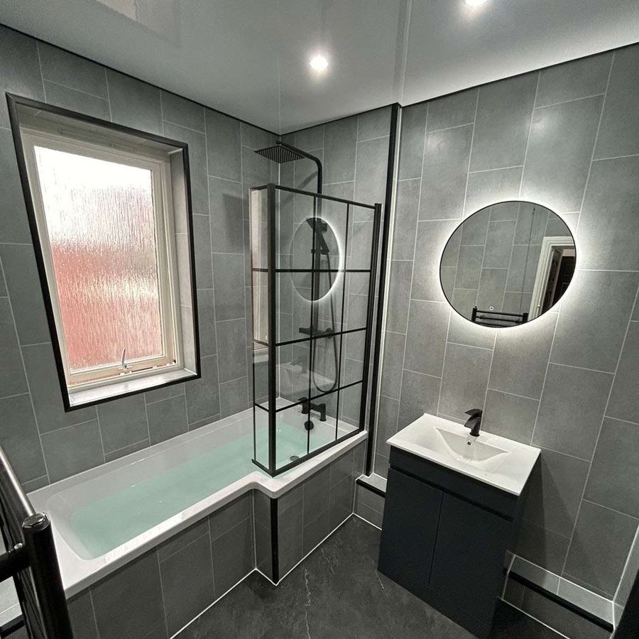 Grey tiled family bathroom with L-shaped bath and illuminated mirror