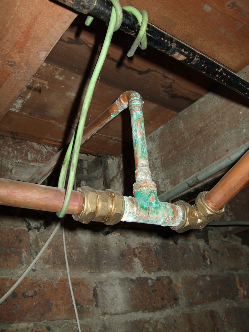 Corroded copper pipework and fittings under a floor