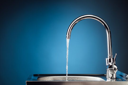 Chrome kitchen mixer tap with water running into a stainless steel sink